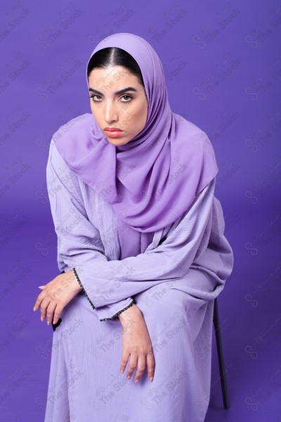 Portrait of a young Saudi woman wearing an abaya and hijab, on a purple background