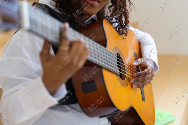 شخص يعزف على الجيتار الكلاسيكي بأصابعه, حيث يبدو تركيزه على الأوتار الخشبية.