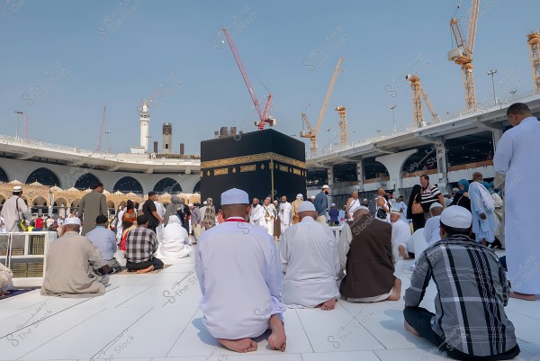 مجموعة من الناس يصلون أمام الكعبة في المسجد الحرام, مع وجود رافعات بناء في الخلفية.