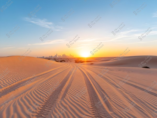 A scenic view of a desert with sand dunes and tire tracks on the sand. A modern city skyline is visible on the horizon under the setting sun, with a blue sky and light clouds.