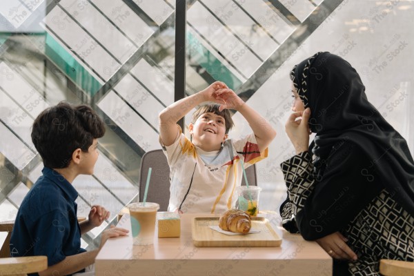 طفلان أحدهما "من ذوي الإعاقة" وامرأة يجلسون على طاولة في مقهى ويستمتعون بوقتهم معاً.