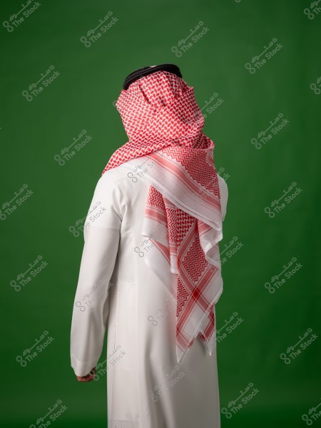 رجل يرتدي الزي الخليجي التقليدي باللون الأبيض والغترة الحمراء واقفًا على خلفية خضراء.