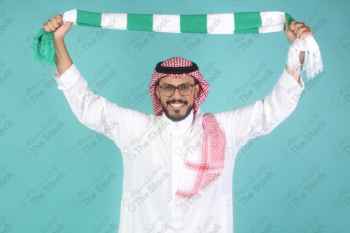 شاب سعودي يرتدي الزي السعودي ممسك شال بيده يقوم بتعابير وجه و يدين تدل على السعادة والحماس ، كأس العالم ، المنتخب السعودي.