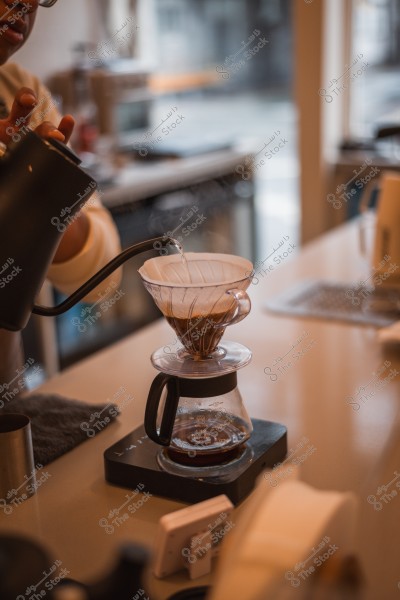 A person pouring hot water from a kettle over coffee grounds in a dripper for making pour-over coffee in a café.