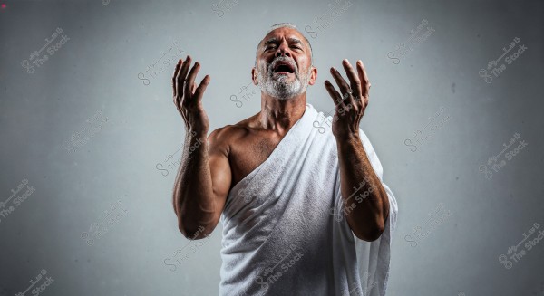 Image of an elderly man with a white beard and mustache, wearing a white cloth draped over one shoulder with his hands raised to the sky in a prayerful position. The background is a neutral gray.