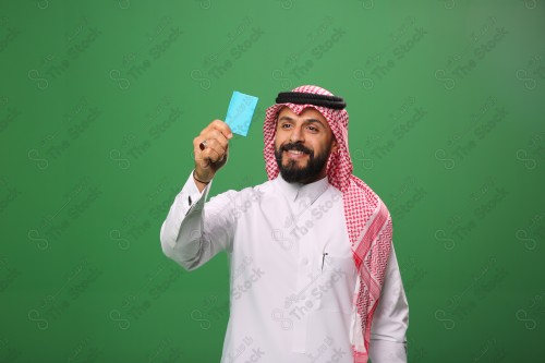 بورتريه رجل سعودي على خلفية خضراء متحمس يحمل بطاقة الصرافة مستعد للتسوق