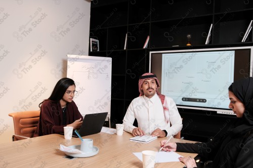 A Saudi man in traditional Saudi dress holds a meeting with Saudi female employees wearing abaya in the meeting room