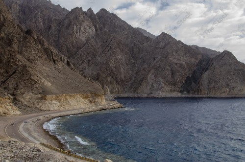 مجموعة من الغيوم فوق سلسلة من الجبال الصخرية و طريق مطل على البحر.