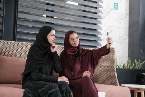 A Saudi woman wearing an abaya holds a mobile phone and displays its screen