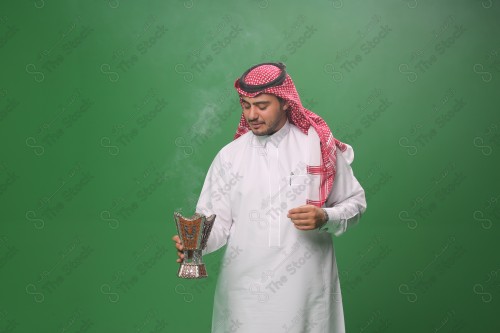 رجل سعودي يرتدي الزي التقليدي على خلفية خضراء ، التطيب بالبخور والعود ، استخدام خشب العود في المناسبات والأعياد.