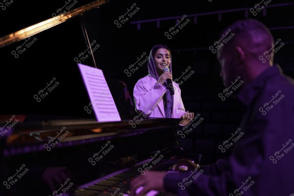 امرأة تغني في الميكروفون أثناء عزف رجل على البيانو في مسرح.