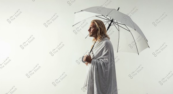 A portrait of a man standing and holding a white umbrella, wearing a white cloth resembling an ihram. The background is open and white, providing a sense of peace and tranquility. The overall appearance reflects a blend of contemplation and calm.