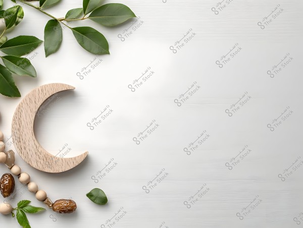 An image showing a white background with a wooden crescent moon decoration on the left side. Next to the moon, there is a string of wooden beads interspersed with dates, and green leaves are scattered around.