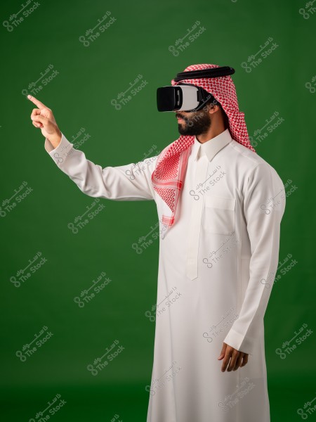 رجل يرتدي ثوبًا سعوديًا ونظارة واقع افتراضي, يقف ويشير بإصبعه في بيئة خضراء اللون.
