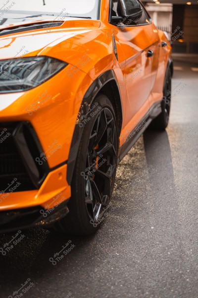 Orange sports car parked on the road, showing details of the front wheel and side panel.