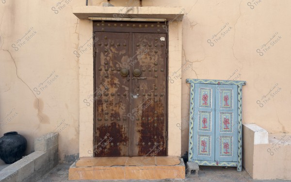 An old wooden door with a colorful wooden window beside it and a black vase.