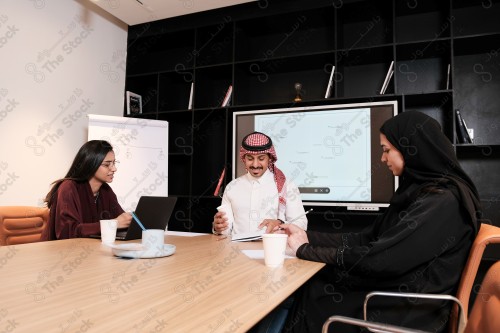 A Saudi man in traditional Saudi dress holds a meeting with Saudi female employees wearing abaya in the meeting room