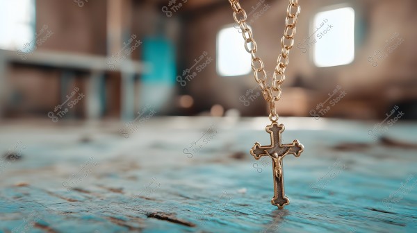 An image of a gold chain with a hanging gold cross, set against a blurred indoor background with indistinct features, and a predominantly blue-grey color on the surface.