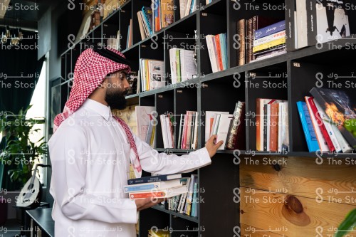 رجل سعودي يرتدي الزي السعودي التقليدي يختار أحد الكتب من المكتبة