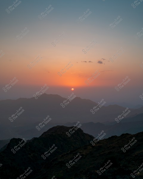 A landscape during sunset showing a blue sky and horizon bathed in shades of orange. Distant mountain peaks stand out with dark shadows in the foreground, conveying a sense of tranquility and natural beauty.