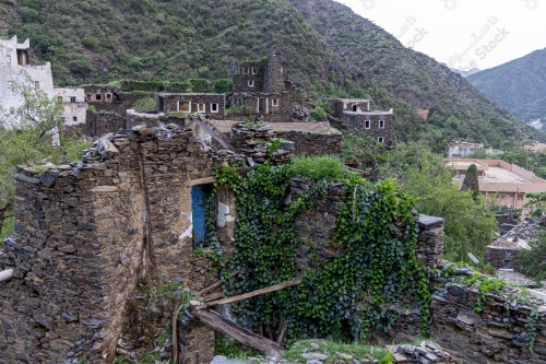 An ancient building built of stones in the middle of a group of windows surrounded by white paint while the sky looks cloudy during sunset, Rijal Almaa Heritage Village in the Asir region