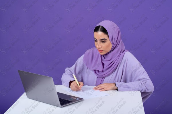 Portrait of a young Saudi woman wearing an abaya and hijab, holding a pen and thinking, against a purple background