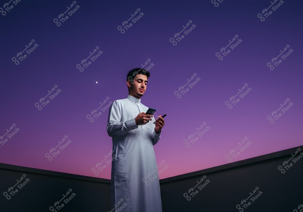 A person wearing traditional attire stands outdoors under a night sky colored in light purple, with a bright planet visible nearby. The individual appears focused on the mobile phone they are holding in their hands.