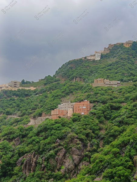 A lush natural landscape with multiple houses nestled among green hills covered with trees and rocks. The buildings are scattered across various levels of the hills. The sky is overcast with clouds, adding a natural ambiance to the scene.