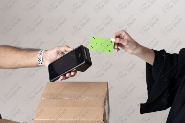 Portrait of a Saudi woman holding a card and making automatic payments, with a cardboard next to her on a white background