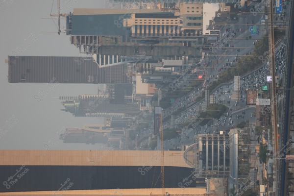 An image of the city of Riyadh in Saudi Arabia, showcasing modern skyscrapers and tall buildings stretching across the city skyline. The image includes prominent business towers and wide roads filled with traffic. The view is captured during the daytime under a hazy sky.