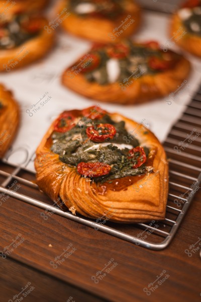 Baked Danish pastry topped with sun-dried tomatoes and spinach, placed on a cooling rack.