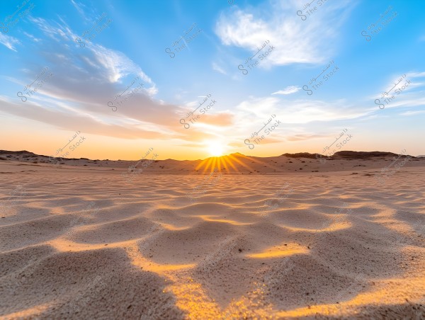A natural landscape depicting a desert sunset. The sand in the foreground glows with a golden hue due to the sunlight. The sky is a blend of vibrant blue, orange, and pink with clouds stretching across the horizon.