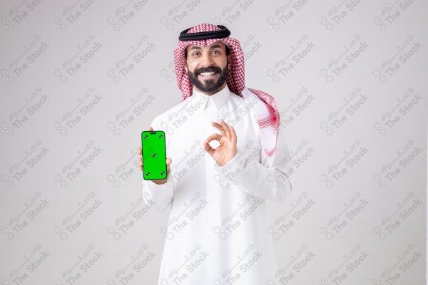 Portrait of a Saudi man holding a phone, pointing at the phone and making different expressions - green screen