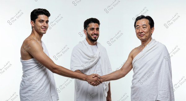 An image of three men standing against a white background, wearing traditional Hajj garments. The men on the sides are dressed in white garments typical for Hajj, while the man in the middle is wearing a traditional white shirt with part of the garment draped over his shoulder like a shawl. They appear to be shaking hands, creating a sense of respect and cooperation.