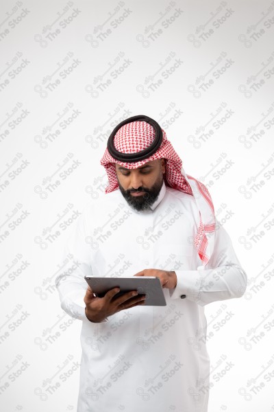 بورتريه رجل سعودي يحمل بيده الآيباد و ينظر لشاشته ويقوم بتعابير مختلفة، خلفية بيضاء