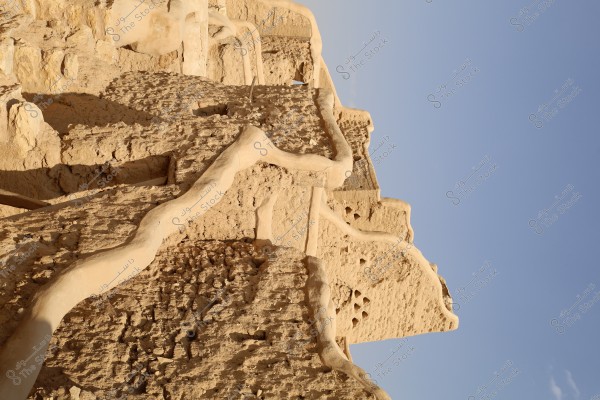 The image shows traditional mud-brick buildings with distinctive architectural shapes. The walls appear to be made of mud with prominent details. The buildings are set against a clear blue sky, suggesting a desert or Gulf region setting.