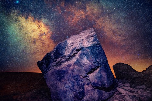 Night shot of a rock in the middle of the desert with stars shining above the Milky Way.