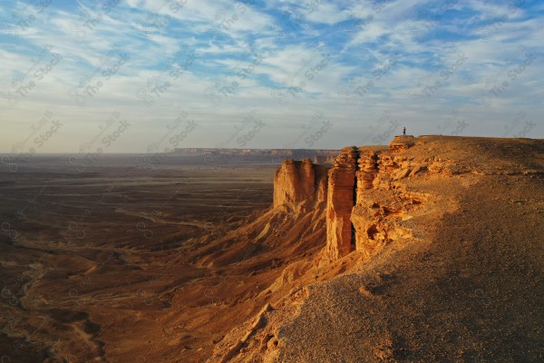 لقطة جوية لسائح يقف على أحد جبال طويق في الرياض والمسمى بحافة العالم في وقت النهار، سلسلة من الجبال الصخرية، تكوينات صخرية، حافة العالم.