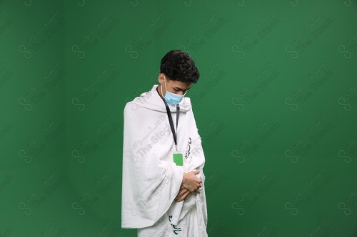 Portrait of a pilgrim with white skin on a green background, wearing Ihram to perform Hajj, performing the duty of prayer