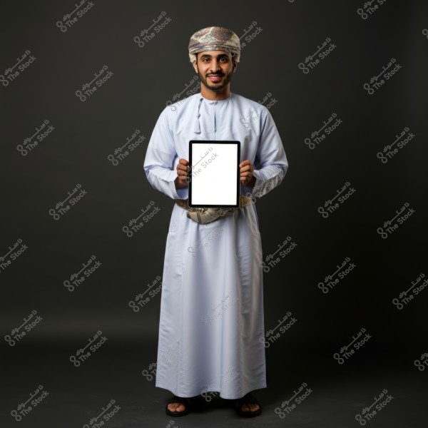 Image of a man wearing traditional Omani attire in white and a patterned turban, holding a tablet with a blank screen. The background is dark gray, and the man is looking directly at the camera with a slight smile.
