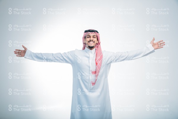 بورتريه رجل سعودي يرتدي الثوب ويقف أمام خلفية بيضاء، يتفاعل بحركات تعبيرية بيديه