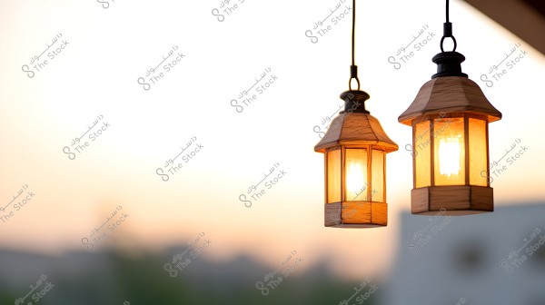 The image shows two hanging lanterns illuminated against a sunset background. The lanterns have a classic design and emit a warm light. The sky in the background appears in a soft orange hue, indicating sunset.
