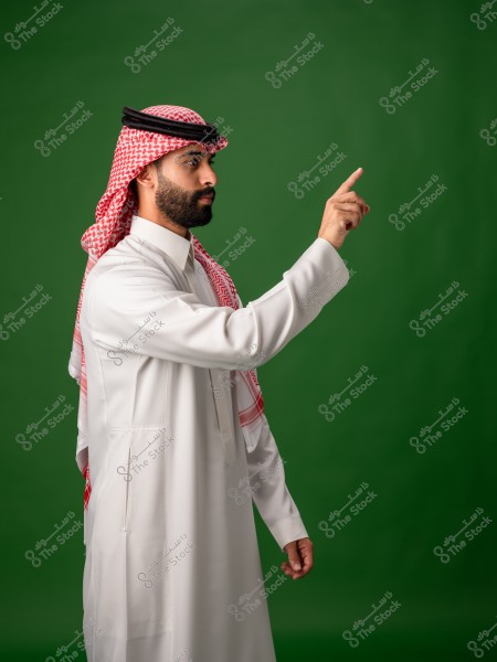 رجل يرتدي الثوب التقليدي السعودي يشير بإصبعه على خلفية خضراء.