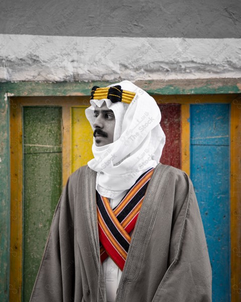 A snapshot of a Saudi man wearing a popular heritage costume on the day of the foundation stands in front of an clay building, heritage uniform, foundation day, old archaeological buildings