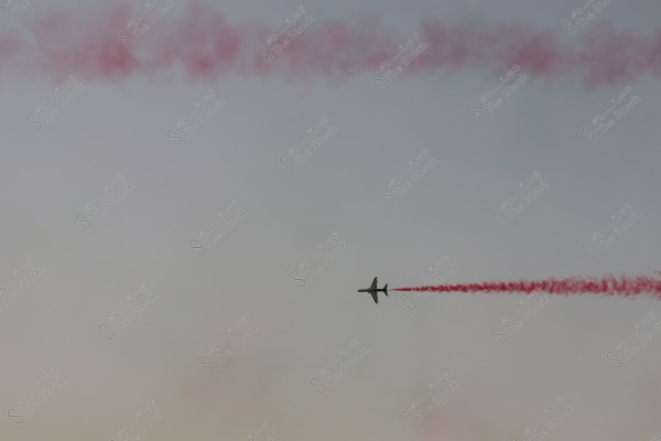 A plane flying in the sky, leaving a trail of red smoke behind.