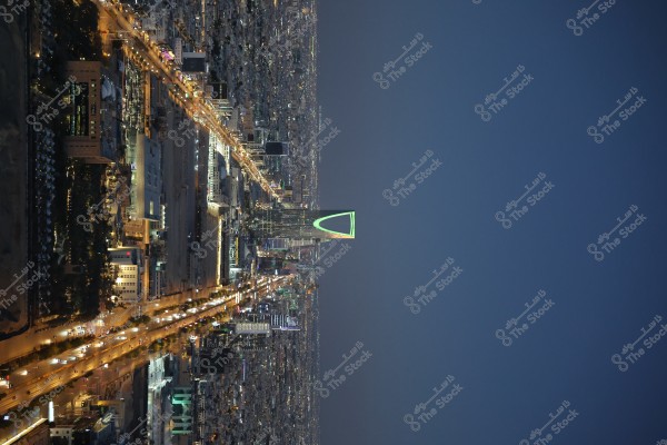 A nighttime image of Riyadh, Saudi Arabia, showing the iconic Kingdom Tower with its green illumination, surrounded by modern buildings and roads bustling with lights.