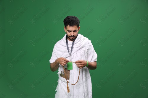 Portrait of a Saudi pilgrim on a green background wearing the Ihram to perform Hajj, holding his rosary in his hand