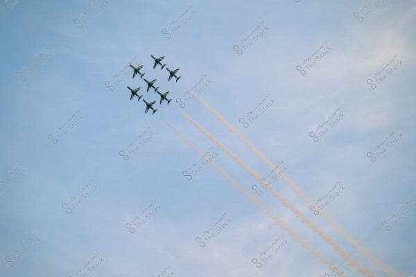 A squadron of six aircraft performs an aerial display in the blue sky. The planes leave long trails of white smoke behind them, arranged in a coordinated formation.