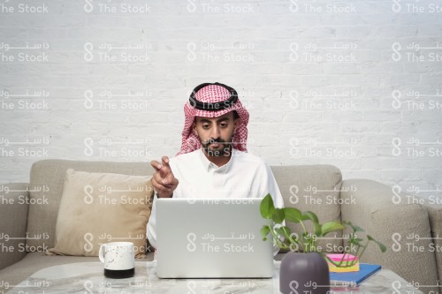 رجل سعودي يرتدي الزي السعودي الرسمي يجلس أمام جهاز الأبتوب يتحدث مع أحدهم بلغة الإشارة