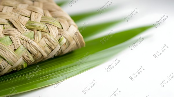 An image of a beautifully woven piece of straw, placed on a shiny green leaf. The weaving displays details of beige and light green colors in an interlocking pattern.